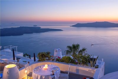 Illuminated candles on table at restaurant in santorini against sky during sunset