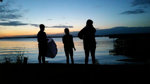 Silhouette people standing by sea at sunset