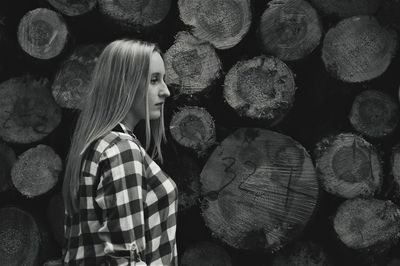 Side view of thoughtful woman standing against logs