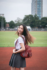 Portrait of young woman wearing backpack while standing on running track