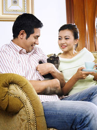 Mid adult couple with coffee pampering cat kitten sofa at home
