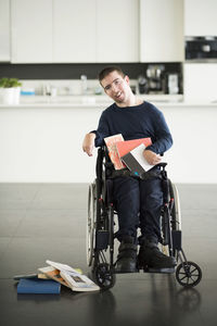 Portrait of disabled man with books on wheelchair at home