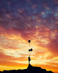 Silhouette of girl holding balloons during sunset