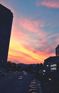 Cars on road in city against sunset sky