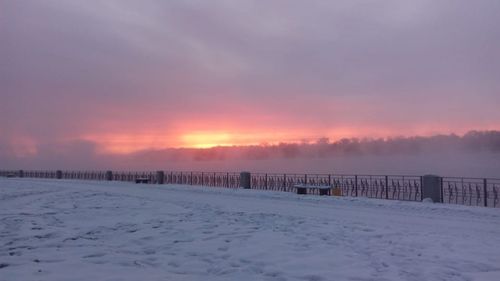 Snow covered field against sky during sunset