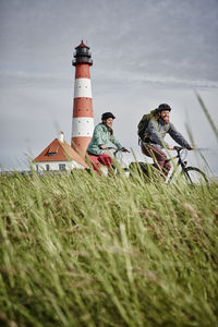 People on field by lighthouse against sky