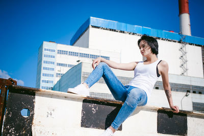 Young woman sitting on barricade against factory