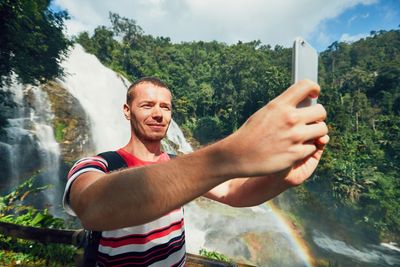 Man taking selfie while standing against waterfall