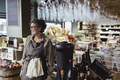 Happy female owner looking away while standing in deli store