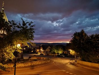 Road by illuminated buildings against sky at night