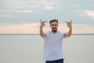 Portrait of man showing middle finger while standing at beach against sky