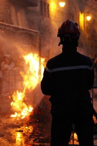 Rear view of male firefighter spraying water on fire at night