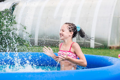 Cheerful little girl with afro-braids splashes water in an inflatable pool on a summer day