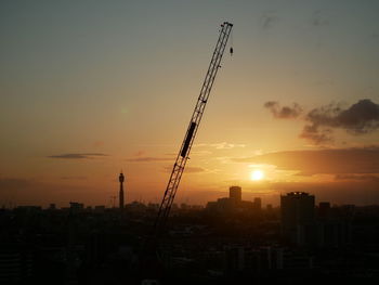 Silhouette of crane at construction site against sky during sunset