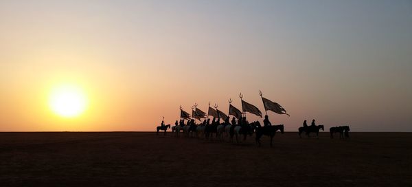 Silhouette people on landscape against clear sky during sunset war