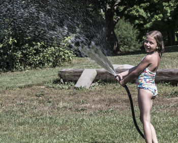 Smiling girl spraying water in lawn with garden hose