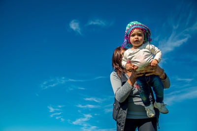 Low angle view of mother and girl standing against blue sky