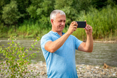 A man stands on the background of a forest and a river and photographs nature.