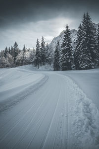 Tire tracks on snow covered land against sky