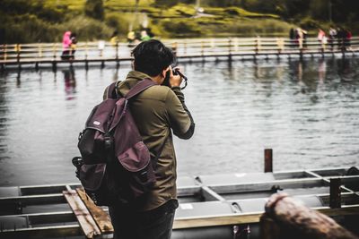 Rear view of man photographing at riverbank