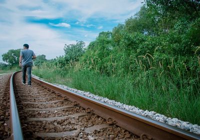 Rear view of man walking on railroad track against sky