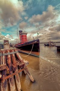 Boats in harbor against cloudy sky