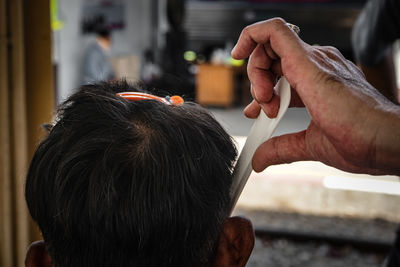 Cropped hand of barber combing male customer hair