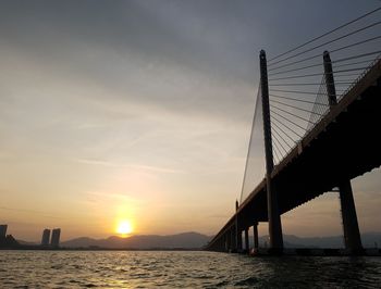 Silhouette bridge over sea against sky during sunset