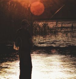 Silhouette man fishing at beach against sky during sunset