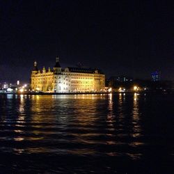 Exterior of illuminated canal in front of river against clear sky at night