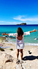 Rear view of woman standing at beach against sky