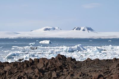 Scenic view of sea by mountain against sky