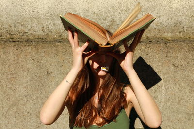 Midsection of woman reading book against wall