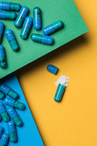 High angle of contents of medical drug poured out of blue colored capsule on yellow background