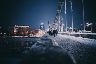 People on street by illuminated buildings against sky at night