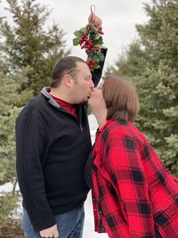 Young couple kissing under mistletoe against trees