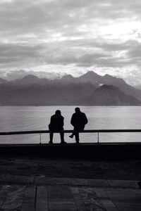 Rear view of silhouette friends standing on lake against mountains