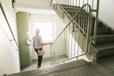 Rear view of woman walking down on staircase in apartment building