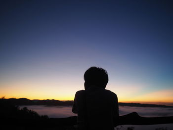 Rear view of silhouette man standing against orange sky