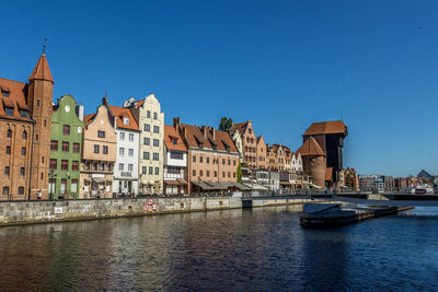 Sailboats in river by buildings against sky