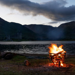 Bonfire in lake against mountains at dusk