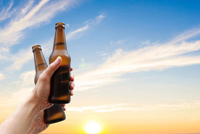 Cropped image of hand holding bottle against sky