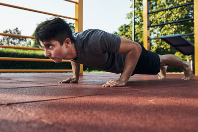 Young man doing push-ups on a red rubber ground during his workout in a calisthenics park