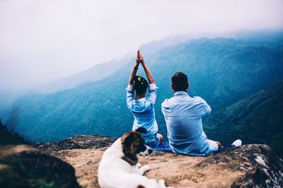 Rear view of man with dog on mountain against sky