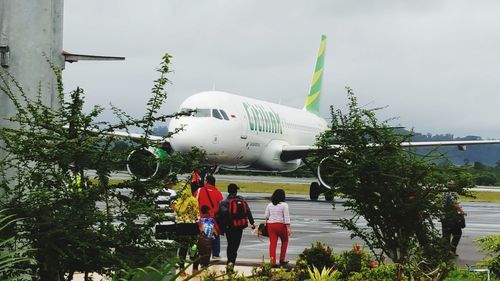 Rear view of people standing by airplane against sky