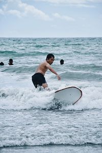 Shirtless man surfing in sea against sky