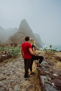 Side view of couple looking at mountain against sky during foggy weather