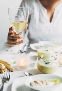 Cropped image of woman holding wineglass with vichyssoise on table