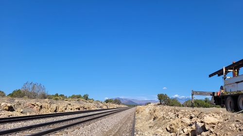 Railroad tracks by road against clear blue sky