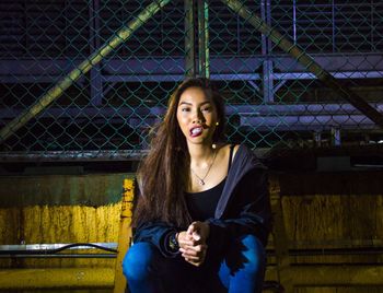 Portrait of smiling woman sitting against by chainlink fence